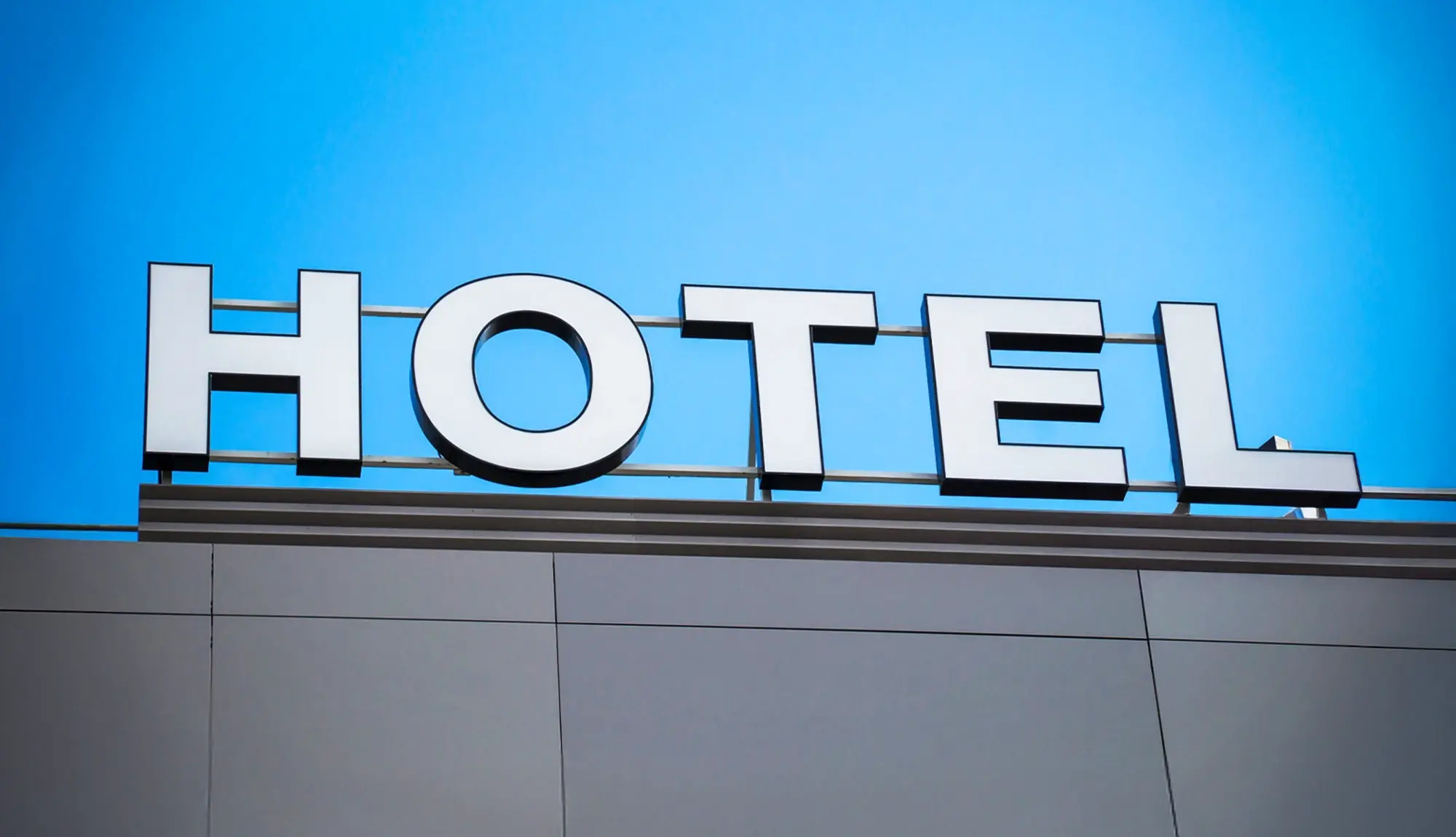 Großer „HOTEL“-Schriftzug auf einem modernen Gebäude vor blauem Himmel.