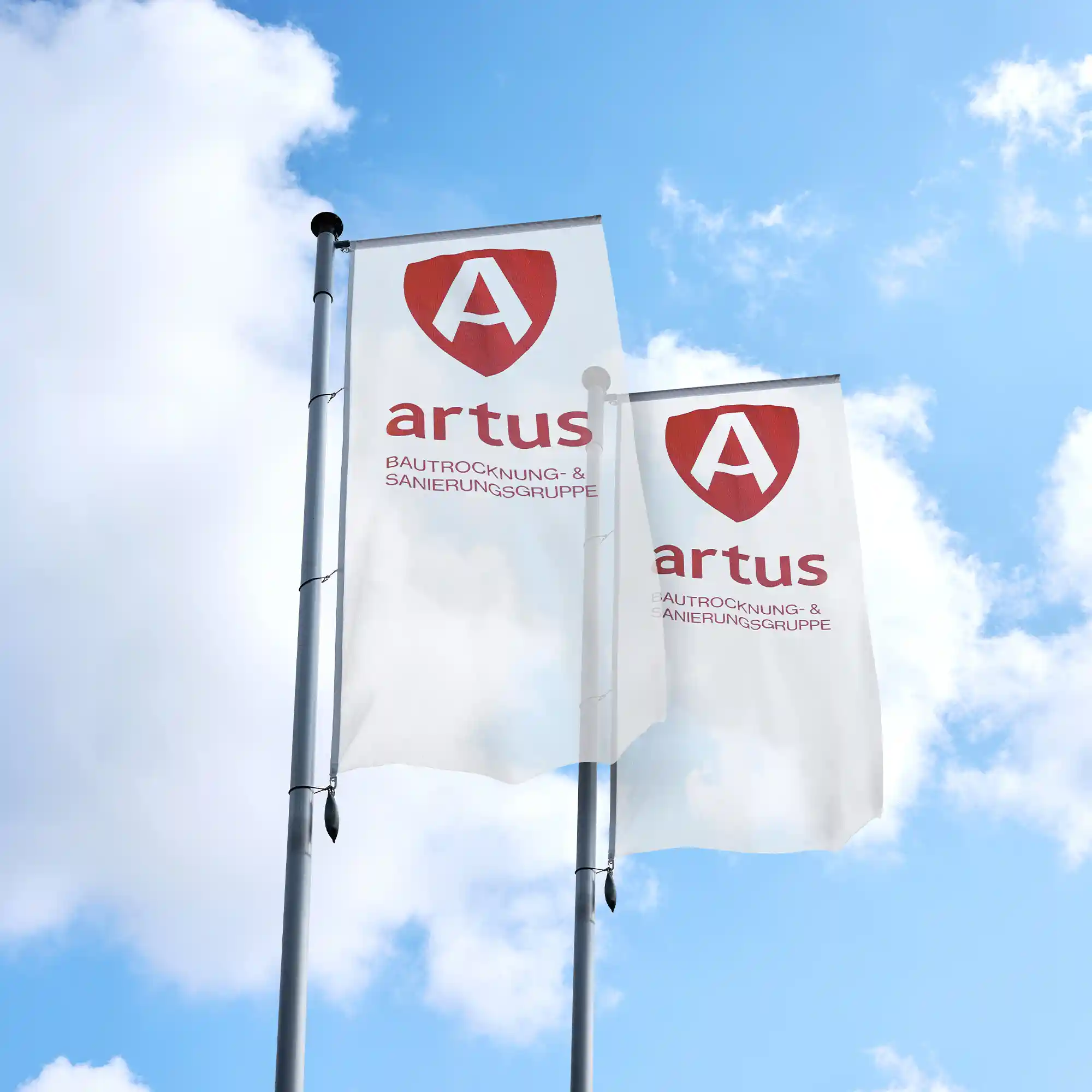 Zwei weiße Werbefahnen der ARTUS Gruppe mit rotem Logo vor leicht bewölktem blauem Himmel.
